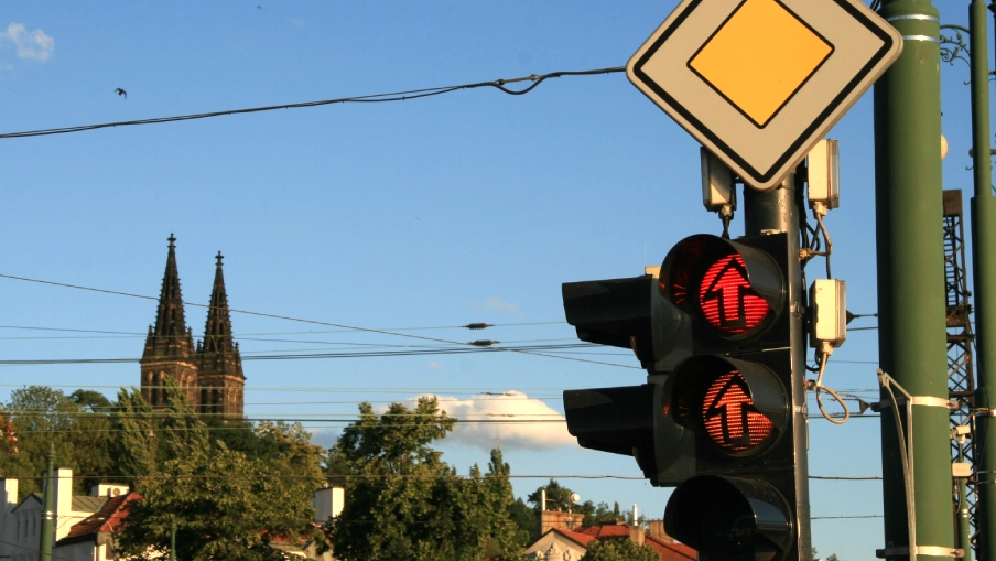 Pohled na semafor z rozsvícenou červenou a oranžovou, v pozadí Vyšehrad v Praze.